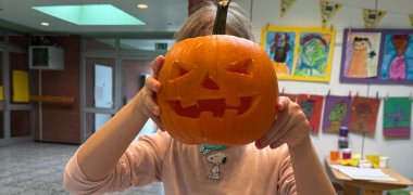 Child holds pumpkin in front of his face